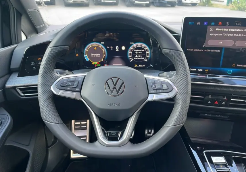 Vue intérieure centrée sur le volant cuir multifonctions R-Line de la Volkswagen Golf E-TSI 150 noire, avec tableau de bord digital.