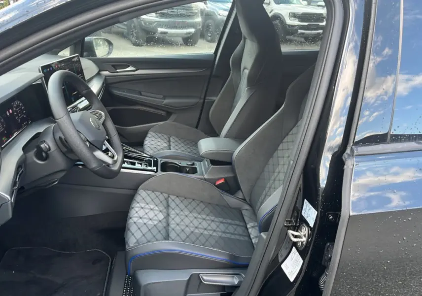 Vue intérieure côté conducteur de la Volkswagen Golf E-TSI 150 R-Line 2026, sièges tissu gris à surpiqûres bleues.