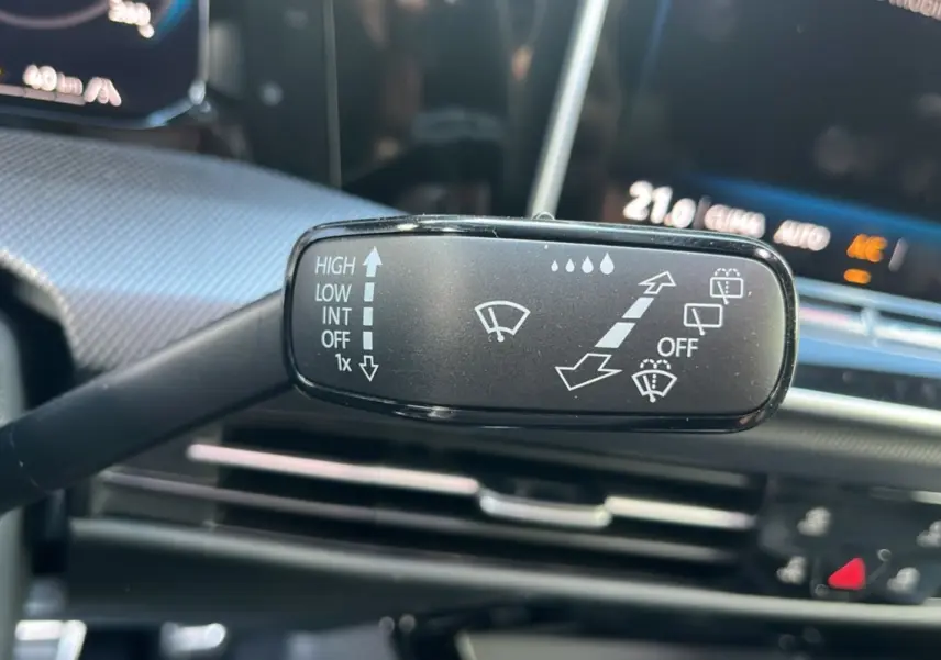 Gros plan sur la commande d’essuie-glace côté gauche du volant d’une Volkswagen Golf noir ébène, tableau de bord en arrière-plan.