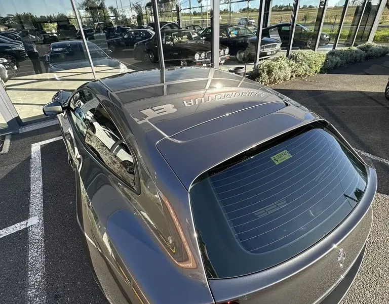 Vue 3/4 arrière d'une Ferrari GTC4 Lusso gris foncé avec feux arrière ronds et toit panoramique réfléchissant.