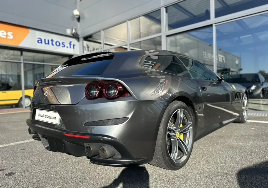 Ferrari GTC4 Lusso gris foncé vue 3/4 arrière droit, avec feux ronds et jantes à cinq branches jaunes.