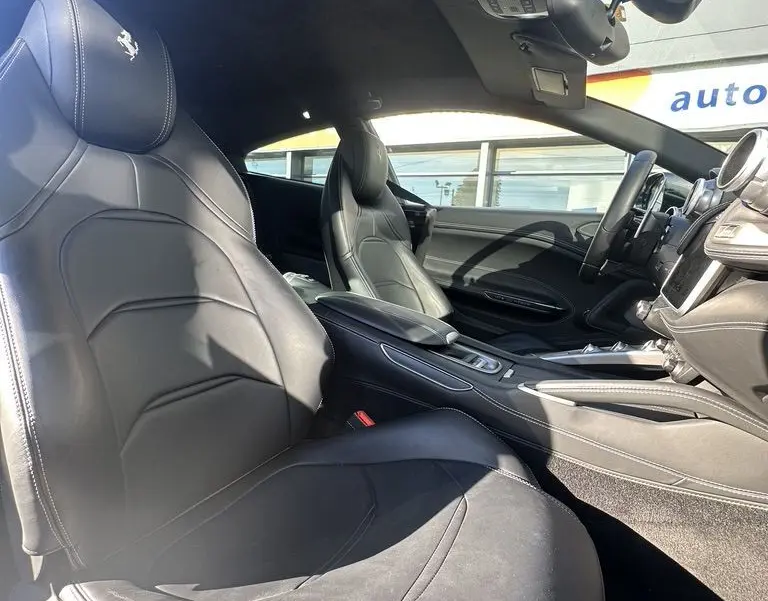 Vue intérieure côté conducteur de la Ferrari GTC4 Lusso 2017 avec sièges en cuir noir et logo cheval cabré brodé.