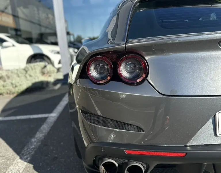 Vue arrière droite d'une Ferrari GTC4 Lusso gris foncé avec feux ronds et double sortie d'échappement visible.