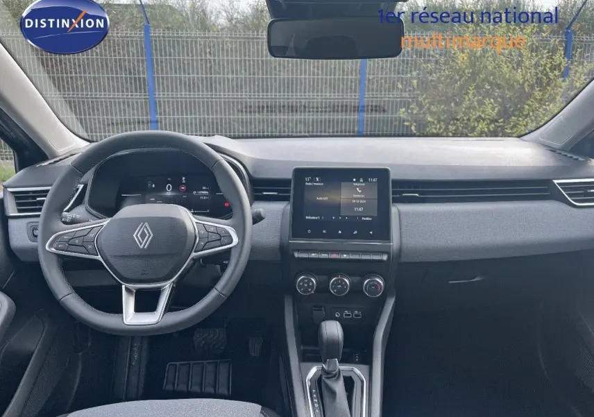 Vue intérieure frontale du tableau de bord et volant de la Renault Clio gris schiste métal 2024 avec écran tactile central et boîte auto.