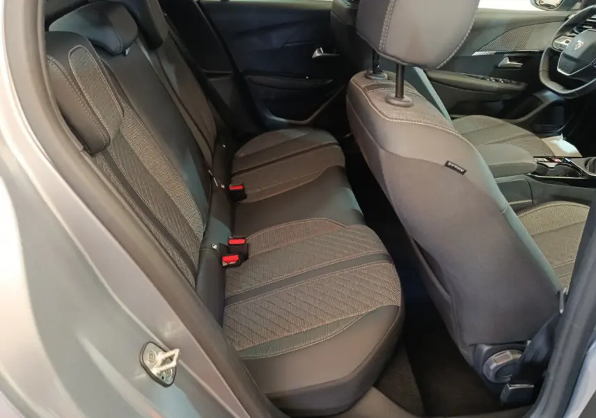 Vue intérieure côté droit montrant les sièges arrière gris clair et partie avant de la Peugeot 208 PureTech 100 S&S Allure 2025.
