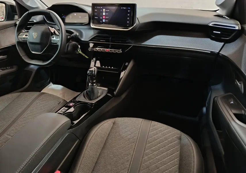 Intérieur de la Peugeot 208 PureTech 100 S&S Allure 2025, vue côté passager avec tableau de bord gris clair et écran tactile.