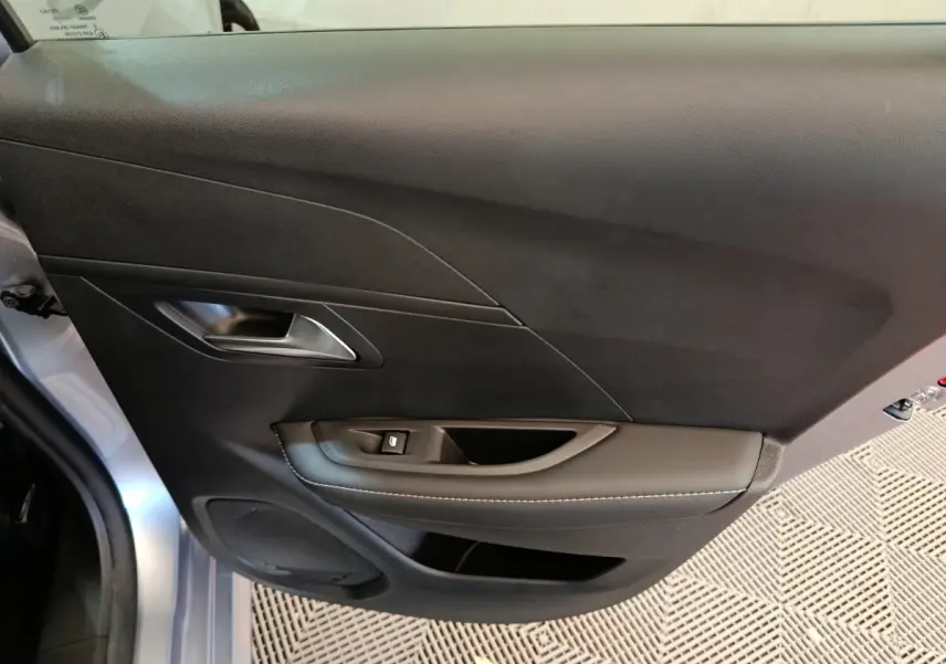 Gros plan sur la porte côté gauche gris clair de la Peugeot 208 PureTech 100 S&S Allure avec poignée et commande de vitre.