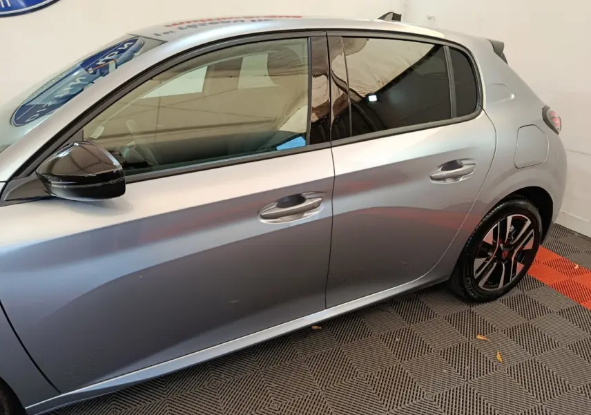 Profil côté gauche d'une Peugeot 208 gris clair 2025 avec rétroviseur noir et jantes alliage modernes.