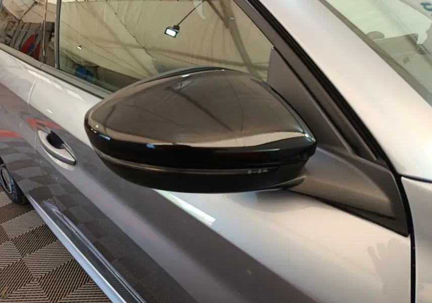 Rétroviseur noir brillant côté gauche sur Peugeot 208 gris clair, vue rapprochée du profil avant du véhicule.