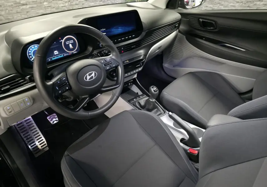 Vue intérieure côté conducteur de la Hyundai Bayon 2025 noire, volant cuir, tableau de bord numérique et levier de vitesses manuel.