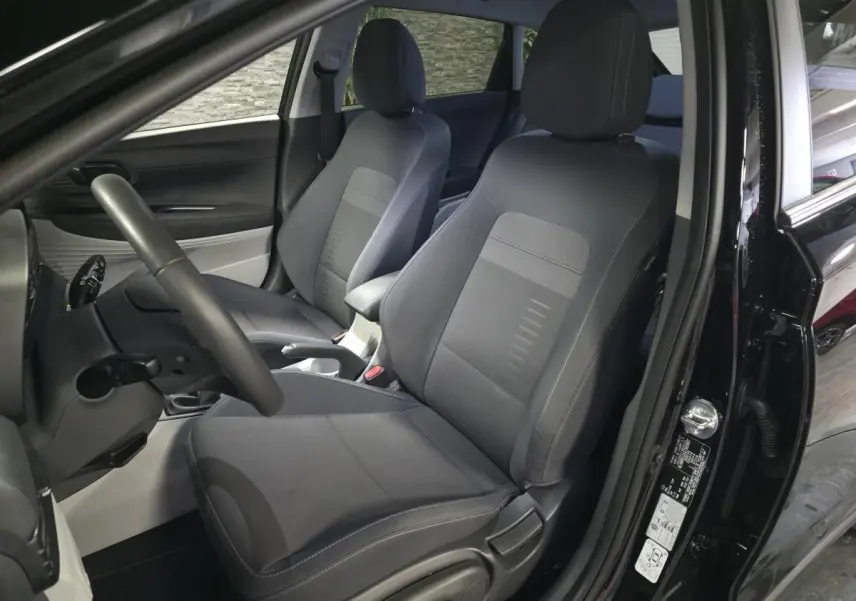 Vue intérieure côté conducteur de la Hyundai Bayon noire 2025, sièges tissu bi-ton gris et noir, volant cuir.