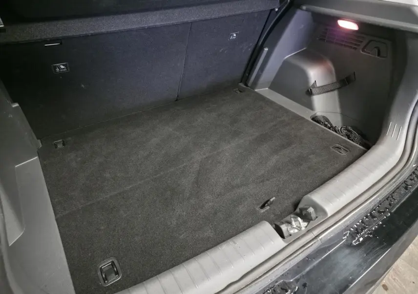 Coffre ouvert vu de l’arrière d’une Hyundai Bayon noire 2025, tapis noir et éclairage intérieur visible.