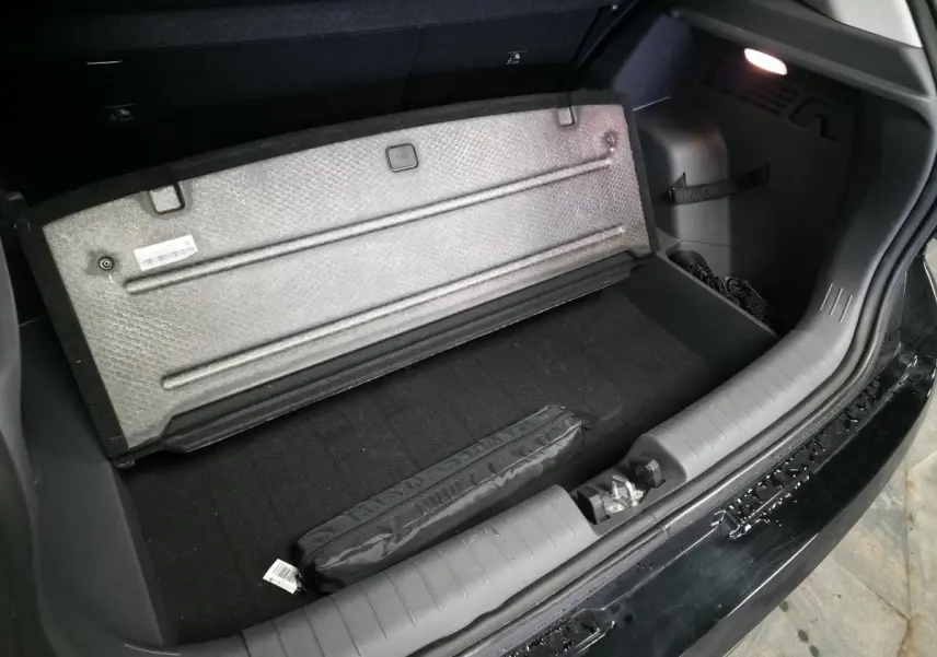 Coffre ouvert d'une Hyundai Bayon noire, vue plongeante sur le plancher et le cache de rangement relevé avec éclairage intérieur allumé.