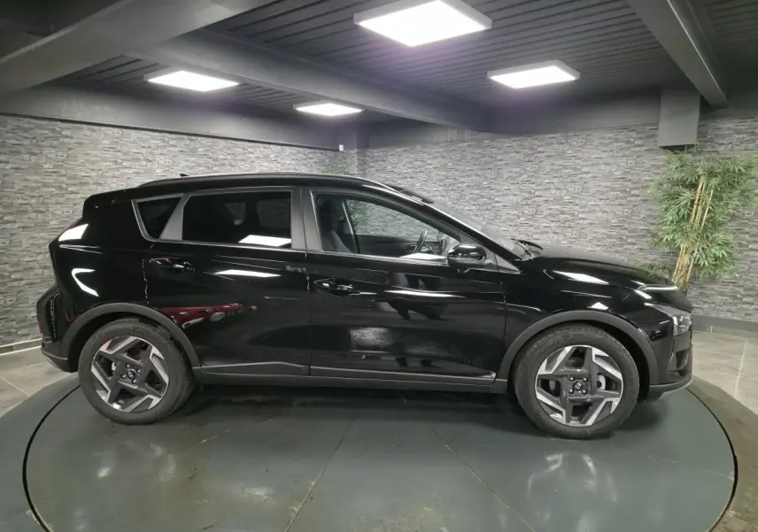 Vue de profil côté gauche d'une Hyundai Bayon 2025 noire métallisée avec jantes alliage 17 pouces dans un showroom.