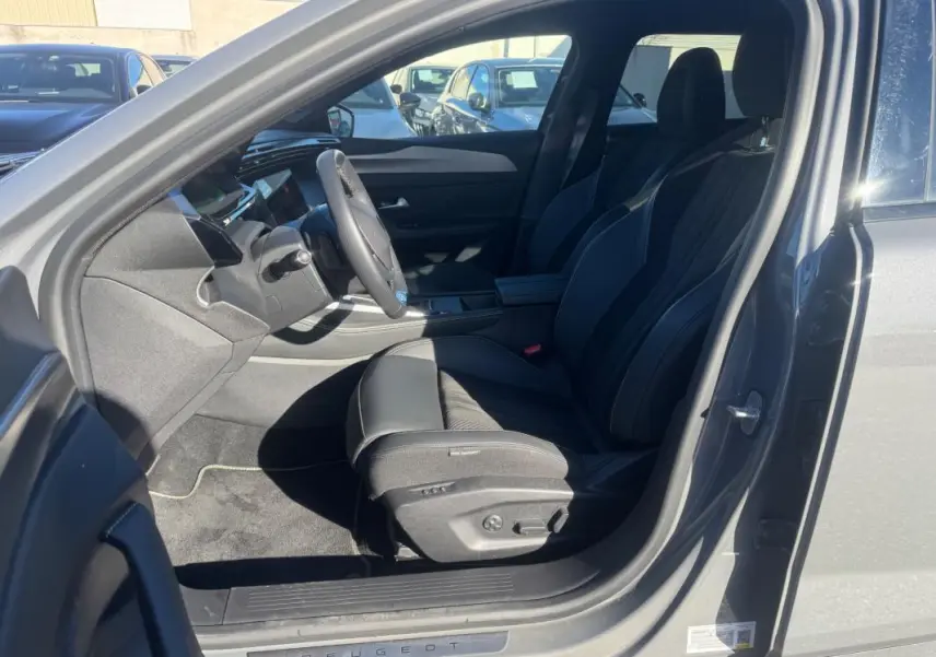 Vue intérieure côté conducteur de la Peugeot 408 Hybrid gris 2024, sièges cuir noirs et volant cuir multifonction.