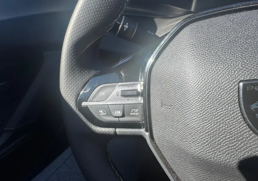 Gros plan sur le volant cuir perforé du Peugeot 408 Hybrid 136 e-DCS6 GT, montrant les commandes intégrées à gauche.