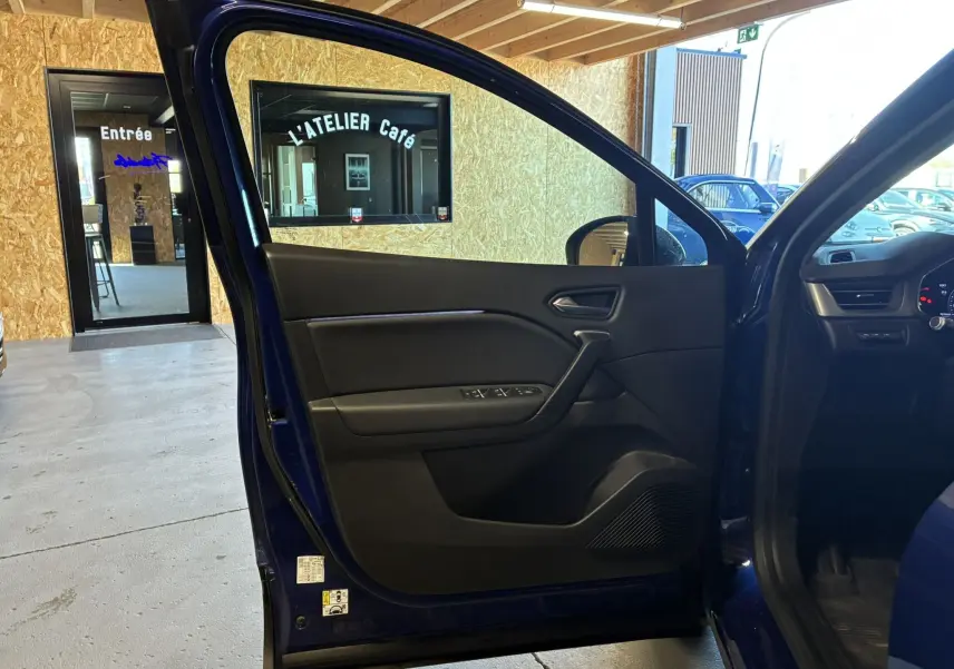 Vue intérieure de la porte avant gauche ouverte d’un Renault Captur bleu 2021, avec panneau de porte noir et commandes visibles.