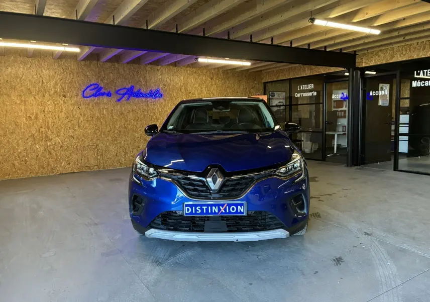Vue de face d'un Renault Captur bleu 2021 dans un showroom avec éclairage intérieur et enseigne néon bleue.