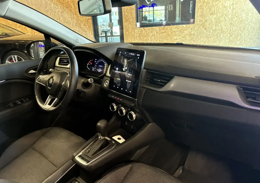 Vue intérieure côté conducteur du Renault Captur bleu 2021, mettant en valeur le tableau de bord et l'écran tactile central.