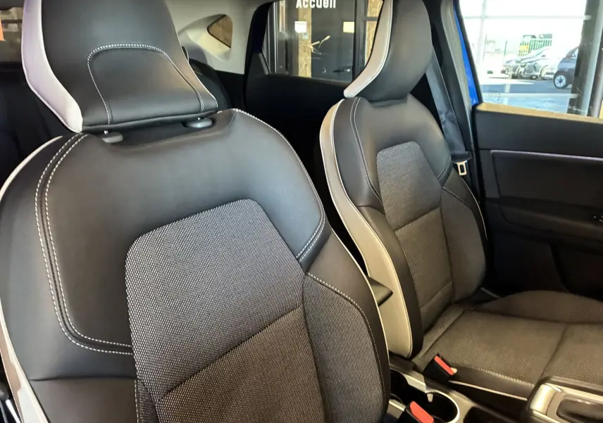 Vue intérieure rapprochée des sièges avant en tissu noir avec surpiqûres blanches du Renault Captur bleu 2021.