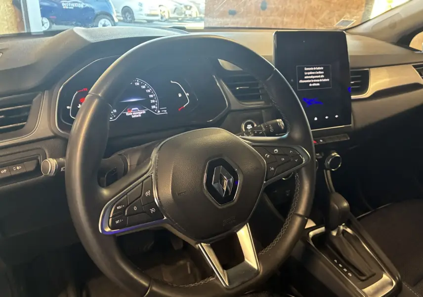 Vue intérieure du poste de conduite du Renault Captur bleu 2021, avec volant multifonction et écran tactile vertical.