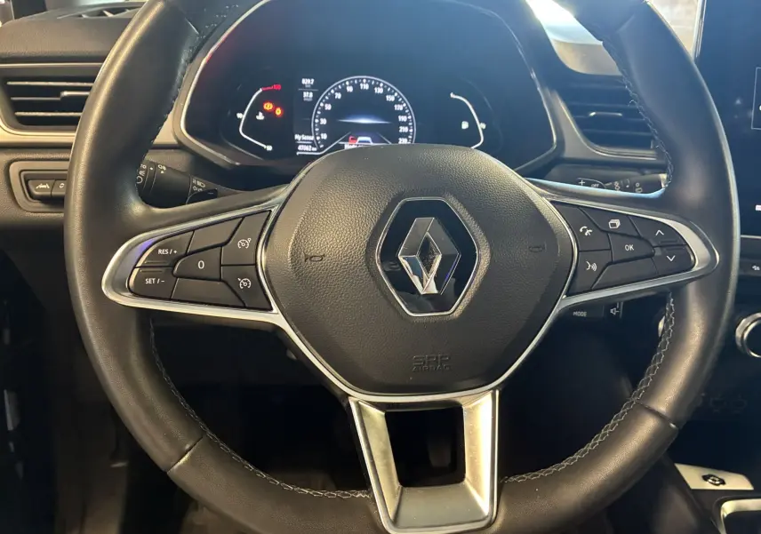 Vue rapprochée du volant noir du Renault Captur 1.3 TCE 140 Intens avec commandes intégrées et tableau de bord digital en arrière-plan.