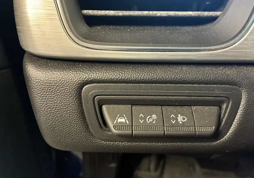 Gros plan sur les commandes d'assistance à la conduite dans un Renault Captur bleu, boutons pour régulateur, phares et maintien de voie.