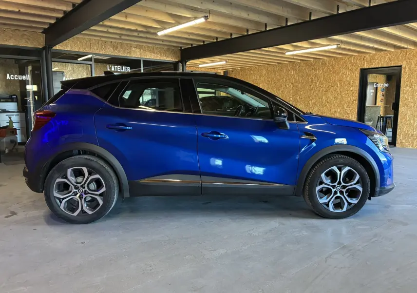 Renault Captur bleu en profil droit dans un garage, avec toit noir et jantes alliage distinctives.
