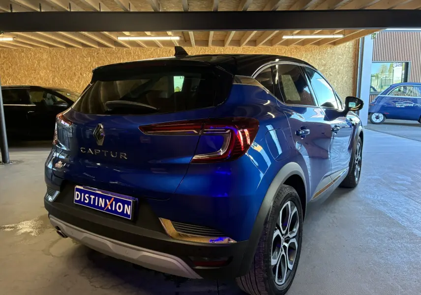 Vue 3/4 arrière droite d'un Renault Captur bleu 2021 avec toit noir et feux arrière LED allumés dans un garage.