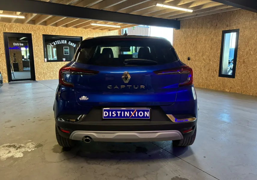 Vue arrière d'un Renault Captur bleu 2021 garé en intérieur, avec logo et feux arrière distinctifs visibles.