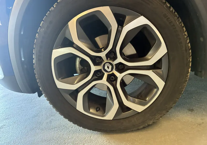 Gros plan sur la roue avant gauche d’un Renault Captur bleu, mettant en valeur la jante alliage noire et argentée au design moderne.