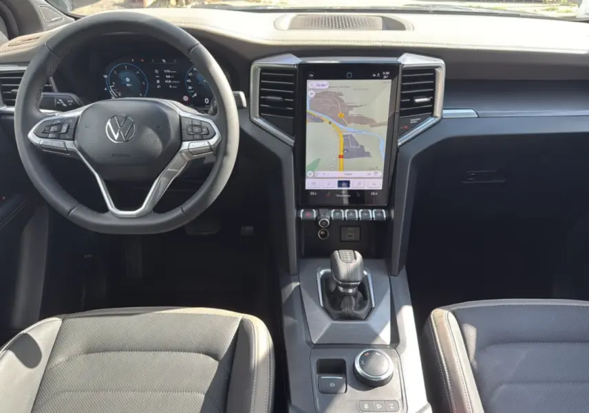 Vue intérieure avant du Volkswagen Amarok 2026 avec tableau de bord noir, écran tactile vertical et volant multifonctions cuir.