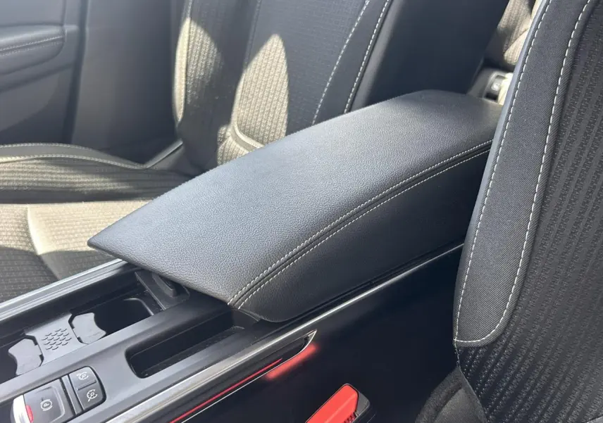 Gros plan sur l'accoudoir central noir et les sièges tissu gris à surpiqûres blanches d'une Renault Mégane IV Intens.
