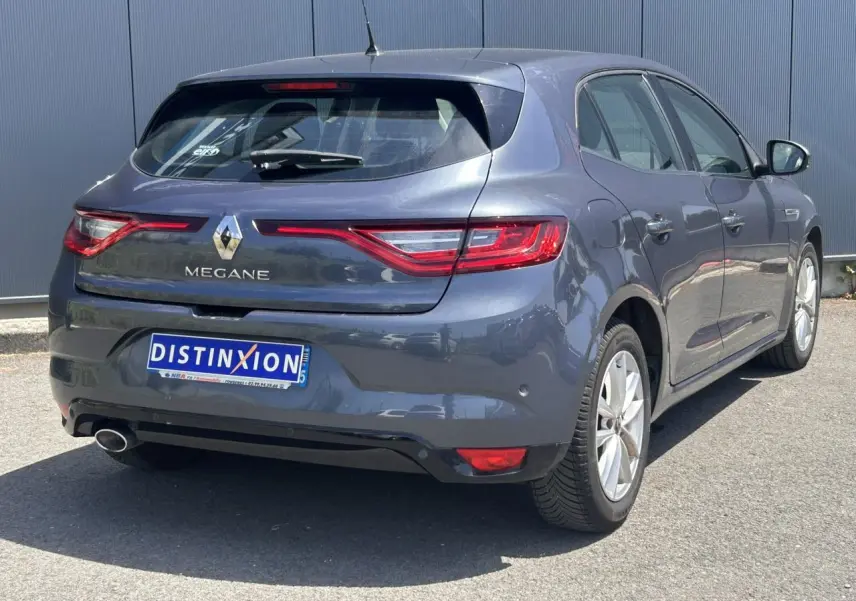 Vue 3/4 arrière droite d'une Renault Mégane IV gris titanium avec feux arrière allongés et sortie d'échappement chromée.