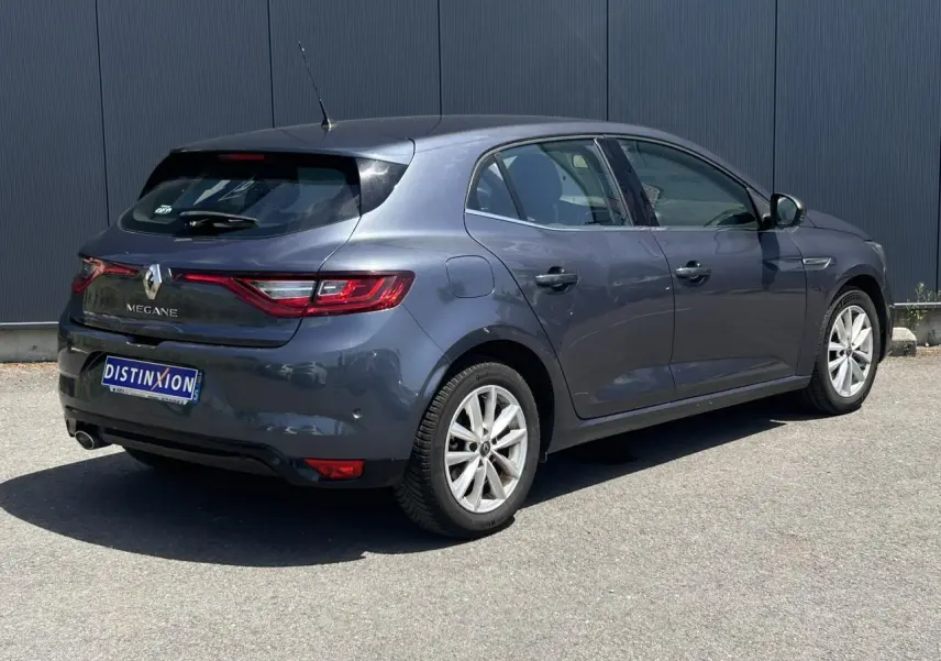 Renault Mégane IV gris titanium vue 3/4 arrière droit, avec jantes 16 pouces et feux arrière LED allumés.