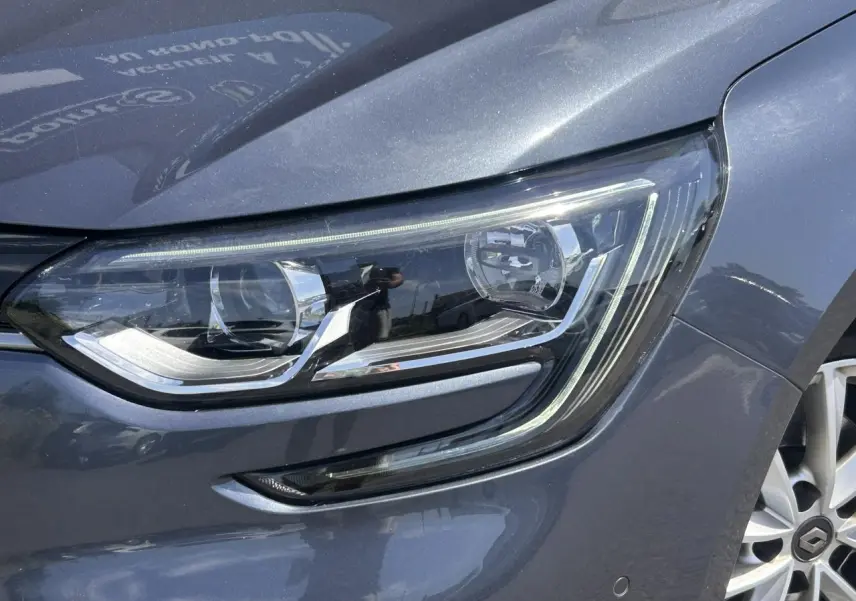 Gros plan sur le phare avant droit de la Renault Mégane IV Gris Titanium avec jante alliage visible.