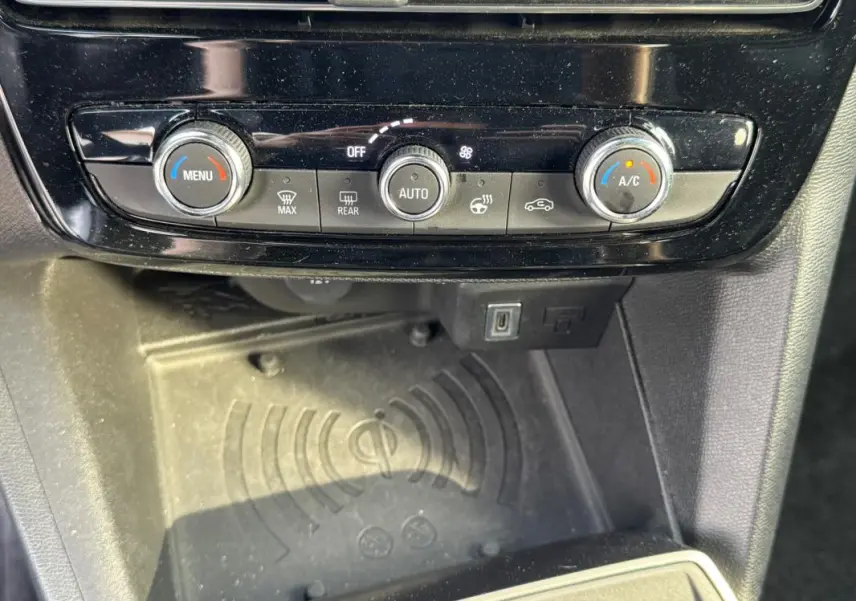 Gros plan sur la console centrale de l’Opel Mokka électrique 2025, montrant les commandes de climatisation et un espace de recharge sans fil.