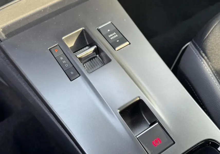 Gros plan sur la console centrale grise de l’Opel Mokka électrique 2025 avec sélecteur de boîte auto et bouton de frein à main électronique.