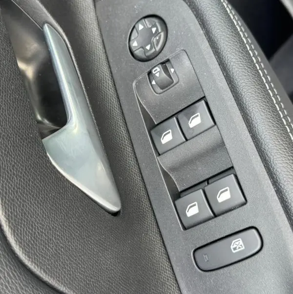 Gros plan sur la commande des vitres et le bouton de réglage des rétroviseurs côté conducteur, intérieur noir de l’Opel Mokka électrique gris.