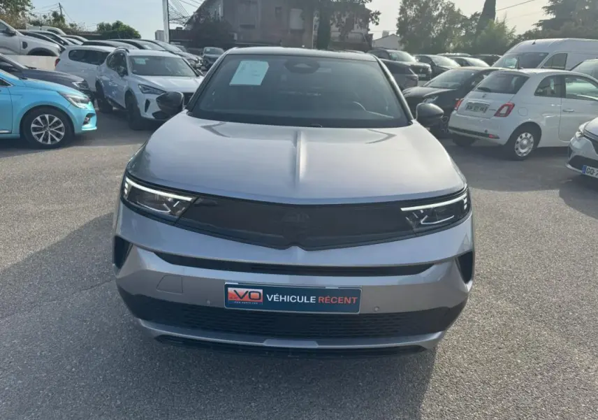 Vue avant d'un Opel Mokka électrique gris 2025 avec calandre noire et phares LED fins, stationné en extérieur.