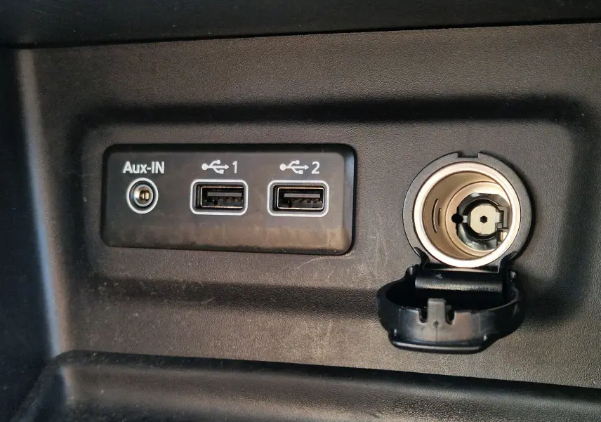 Gros plan sur les ports USB doubles, prise Aux-IN et allume-cigare du tableau de bord d'une Renault Mégane blanche.