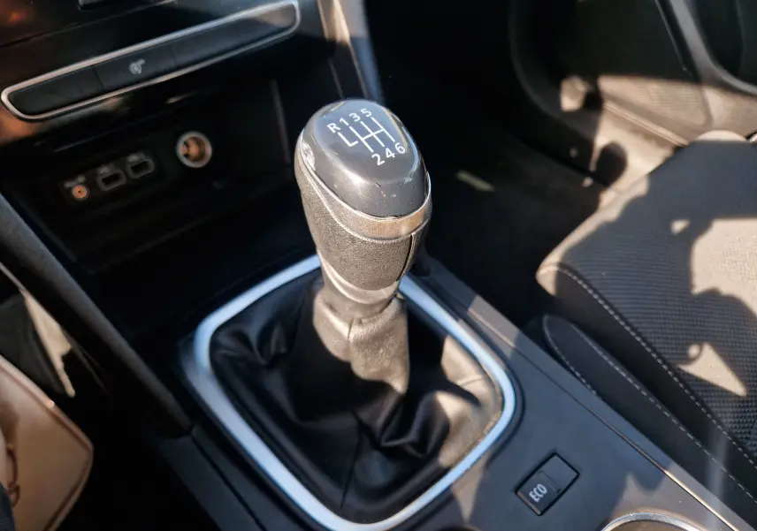 Gros plan intérieur sur le levier de vitesses manuel noir de la Renault Mégane blanche, avec bouton ECO visible à droite.