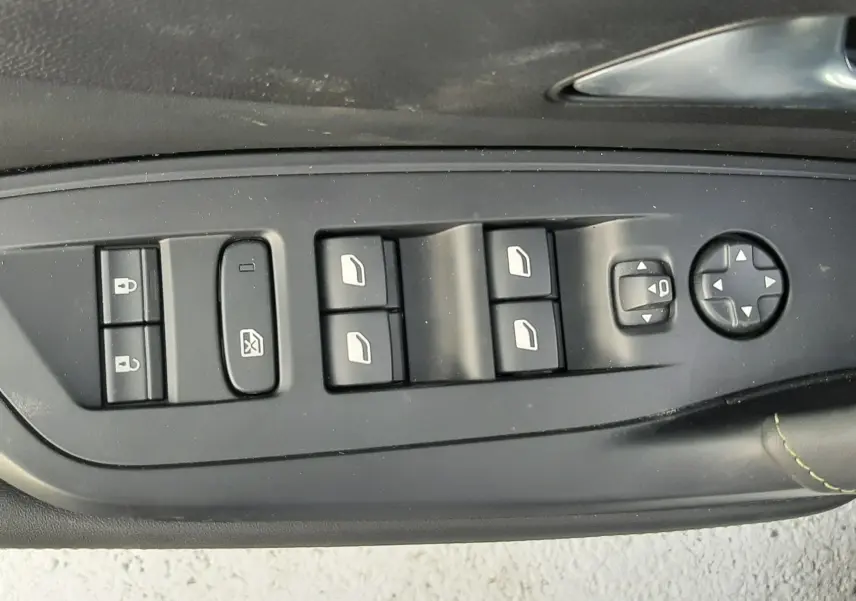 Vue rapprochée des commandes de lève-vitres et réglage des rétroviseurs côté gauche d’une Peugeot 308 SW blanche 2024.