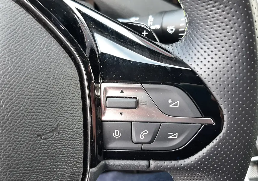 Gros plan sur les commandes multifonctions côté droit du volant perforé noir du Peugeot 308 SW blanc Okenite 2024.