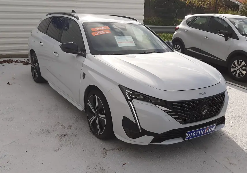 Peugeot 308 SW blanc Okenite vue 3/4 avant droit, calandre noire distinctive et jantes alliage bicolores.