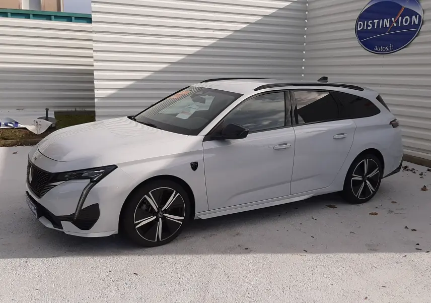 Peugeot 308 SW blanc Okenite vue 3/4 avant droit, jantes noires et toit ouvrant panoramique visible.