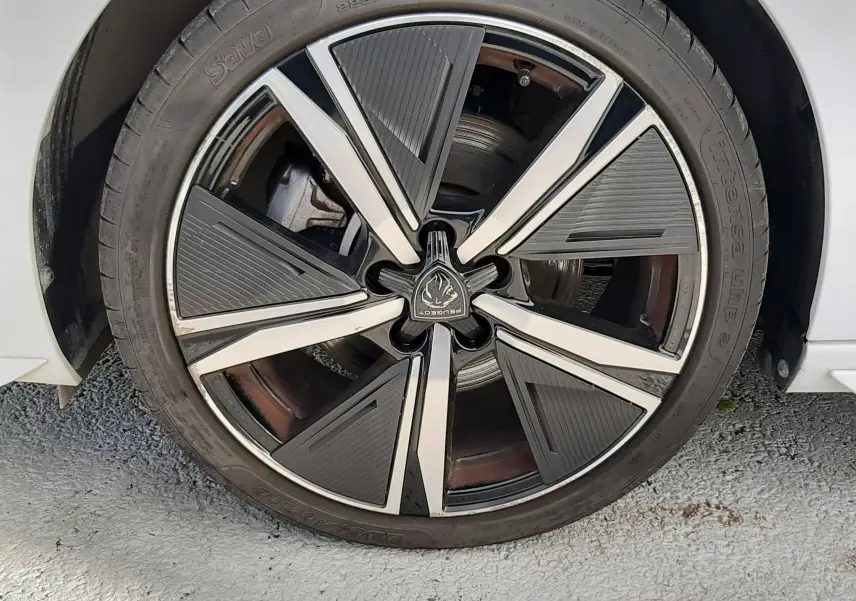 Gros plan sur la roue avant droite d’une Peugeot 308 SW blanche, avec jante alliage noire et argentée au design moderne.