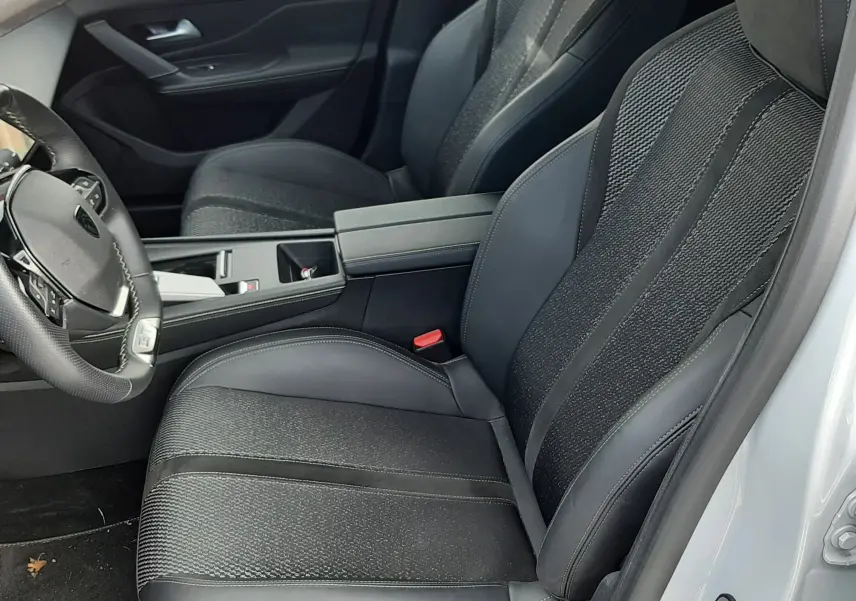 Vue intérieure côté conducteur de la Peugeot 308 SW 2024 blanc Okenite, sièges sport noirs avec logo Peugeot brodé.