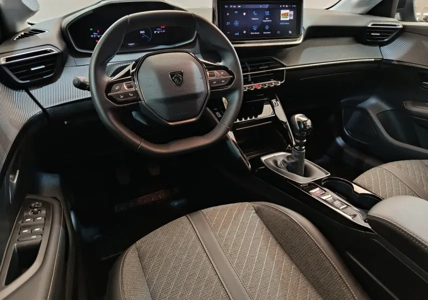 Intérieur de la Peugeot 208 PureTech 100 S&S Allure 2025, vue côté conducteur, volant cuir et console centrale avec boîte manuelle.