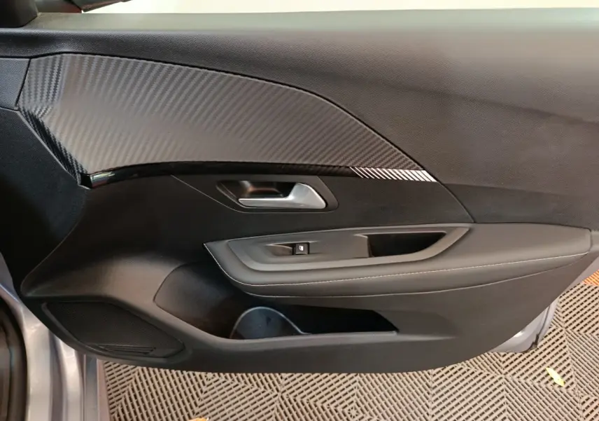 Vue côté gauche de la porte intérieure noire avec insert effet carbone d'une Peugeot 208 gris clair 2025 PureTech Allure